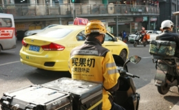 Pengantar barang berjaket kuning mengendarai skuter di jalan