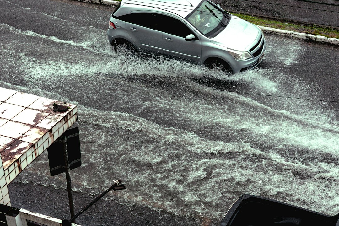 Mobil perak melintasi jalan tergenang banjir hingga air memercik